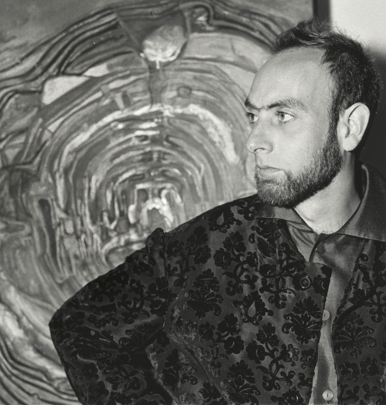 Hundertwasser wearing a very cool damask flocked jacket, standing in front of one of his paintings